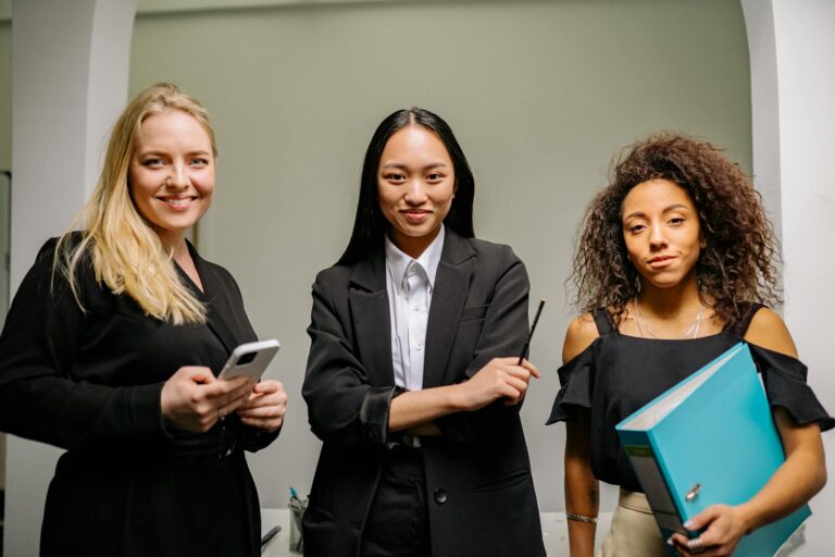 Three diverse women confidently posed in a modern office space.