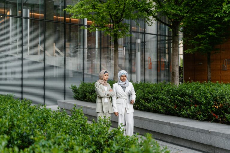 Two Muslim women in corporate attire discuss business outdoors in a modern city environment.